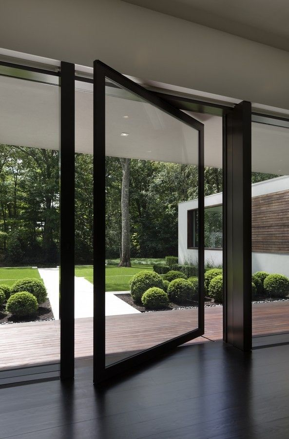 Porta de vidro pivotante com esquadria preta aberta para um jardim